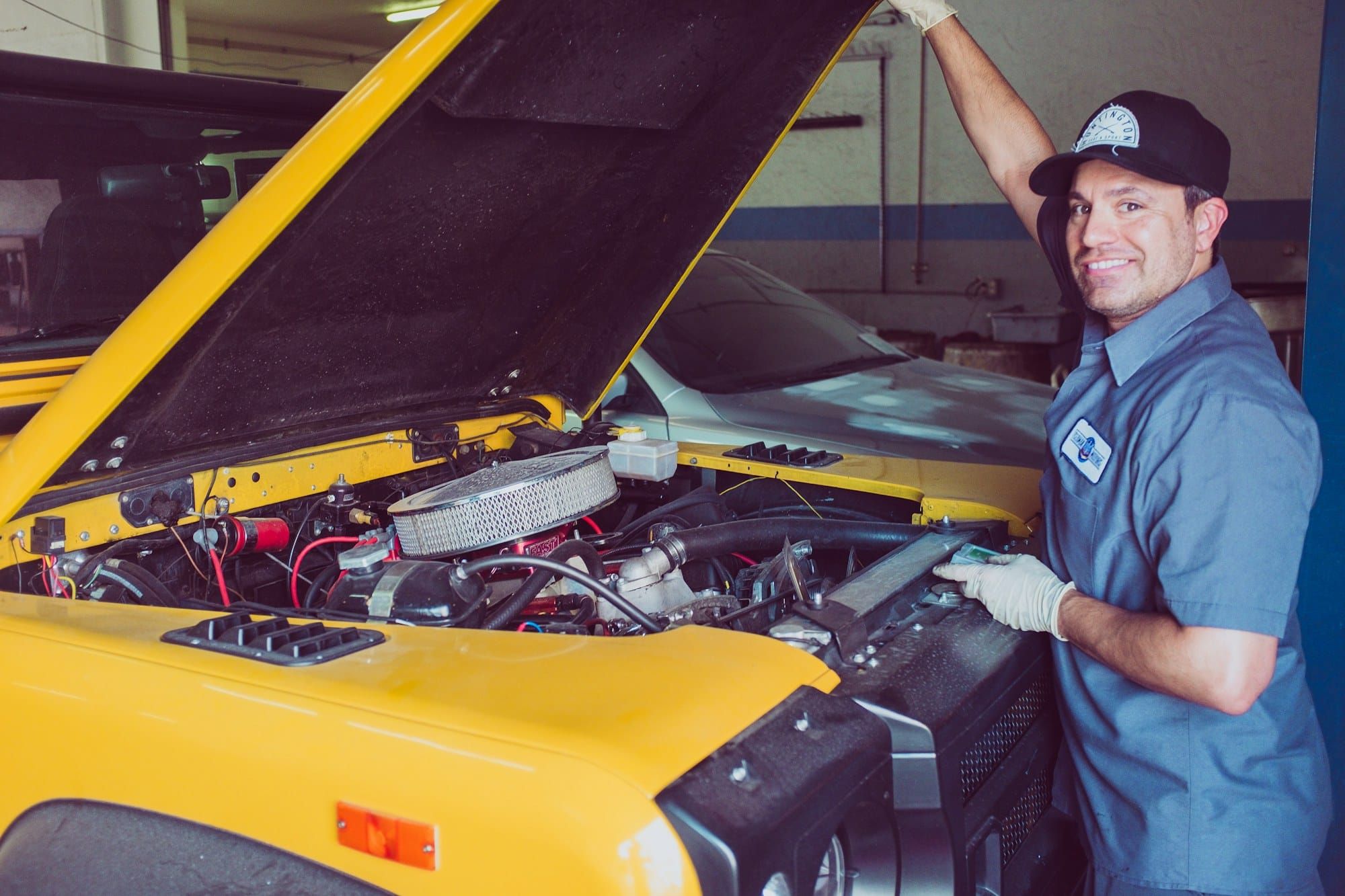 Mecânico sorrindo ao lado do motor de um carro (foto ilustrativa)